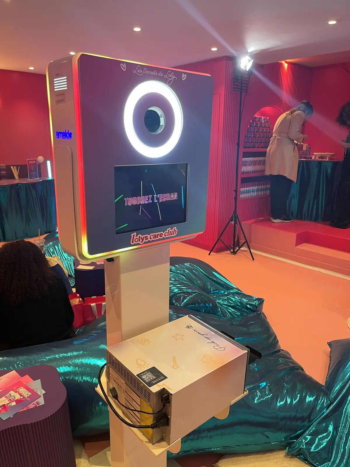 La borne photobooth Smakk habillée aux couleurs d'une marque, imprimante au pied, dans un salon aux murs rouges