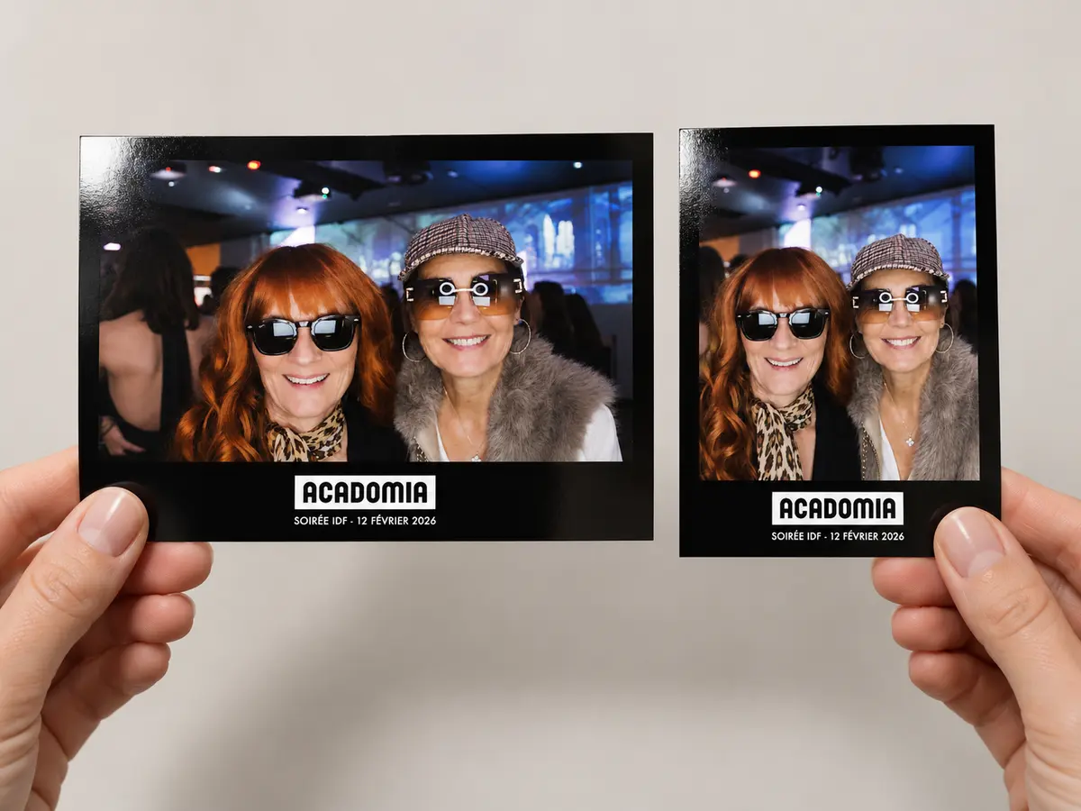 Deux tirages photobooth tenus en main, cadre noir au nom du client et date de la soirée imprimés sous la photo