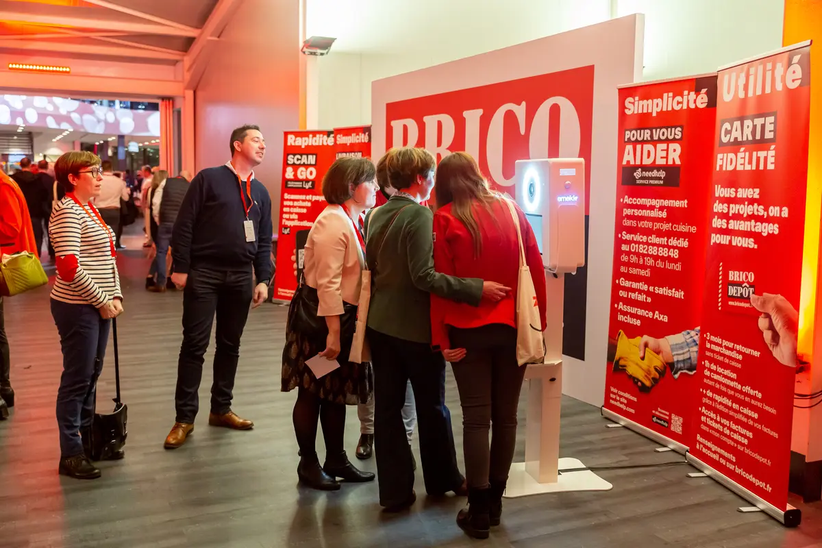 Stand Brico Dépôt rouge sur Batimat avec une borne photo Smakk entre les kakémonos et des visiteurs dans l'allée